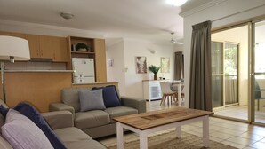 A modern living room with a sofa, a coffee table, and a dining area with a table and chairs. - Central Plaza Port Douglas Apartments (Port Douglas)