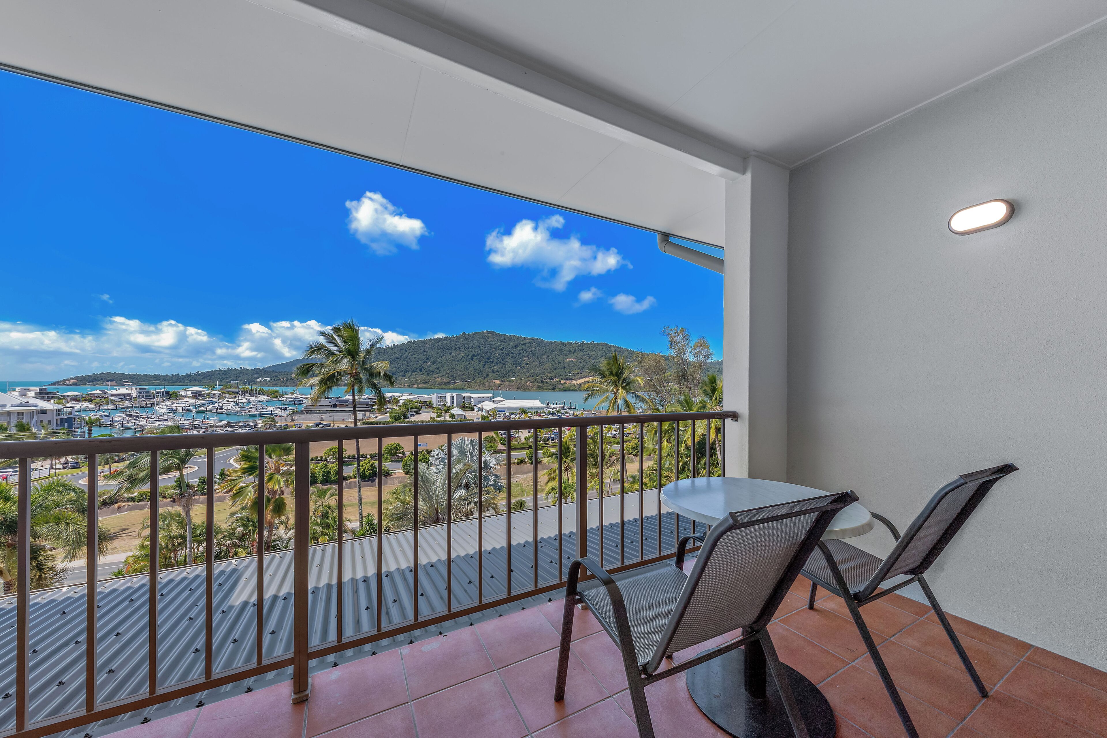A balcony with a table and chairs, overlooking a marina and a mountainous landscape.