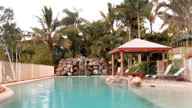 A pool with a waterfall, lounge chairs, and a gazebo. - at Boathaven Bay Holiday Apartments (Airlie Beach)