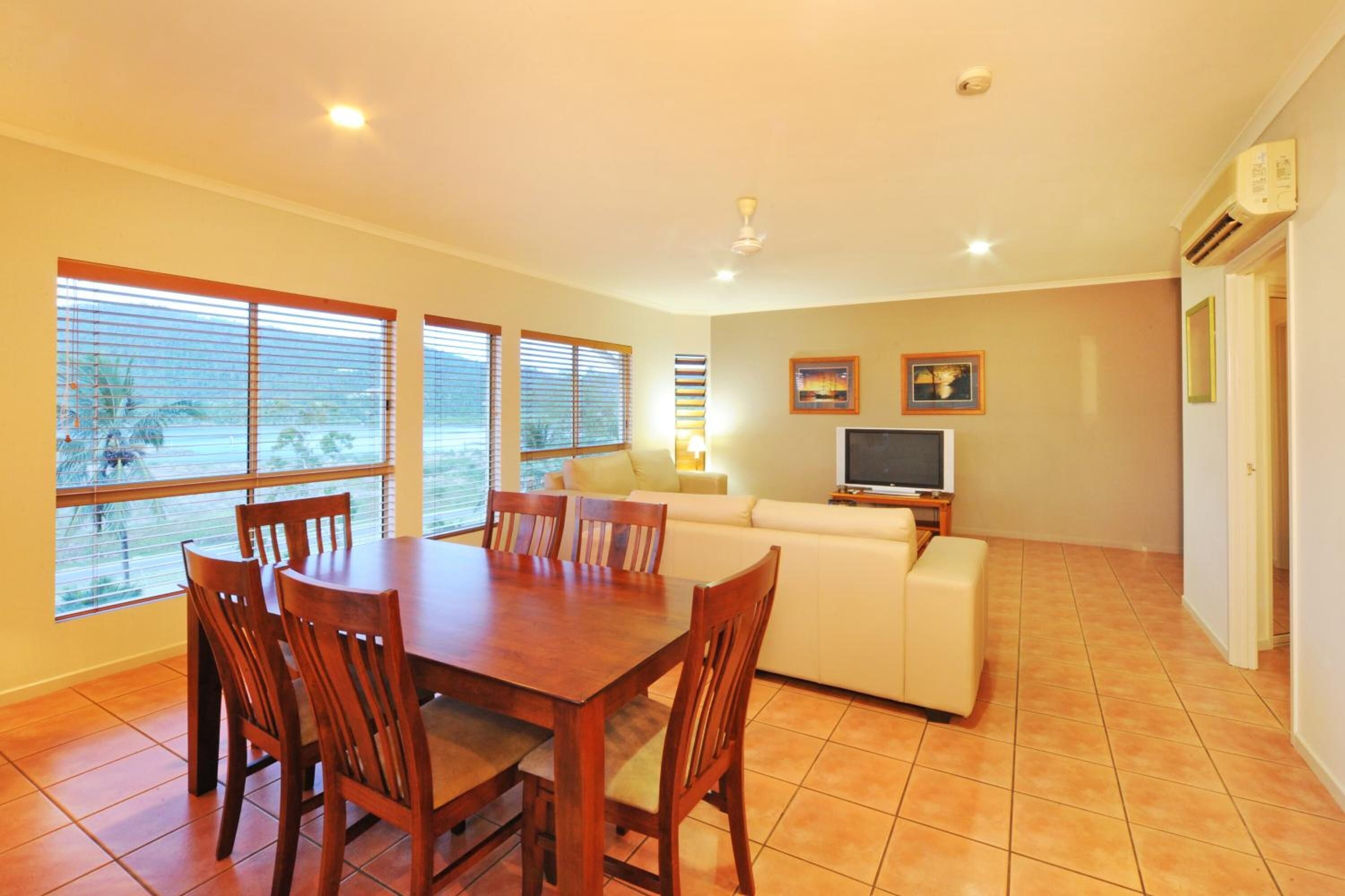 Amplia sala de estar con mesa de comedor, sofá blanco y televisor.