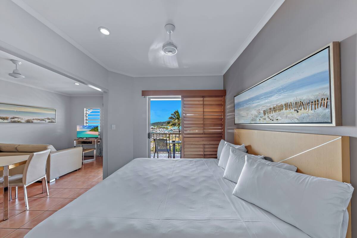 A hotel room with a large bed, a desk, a chair, a television, and a balcony with a view.