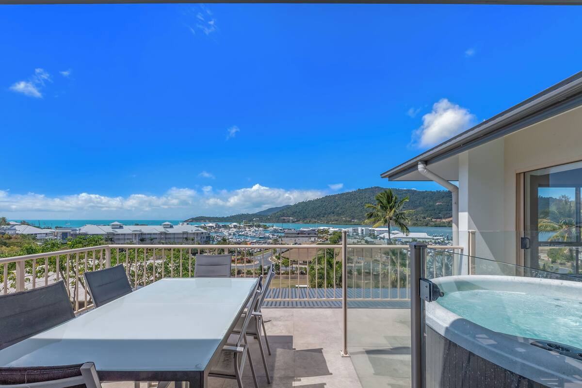 A balcony with a table and chairs, a hot tub, and a view of the sea and buildings.