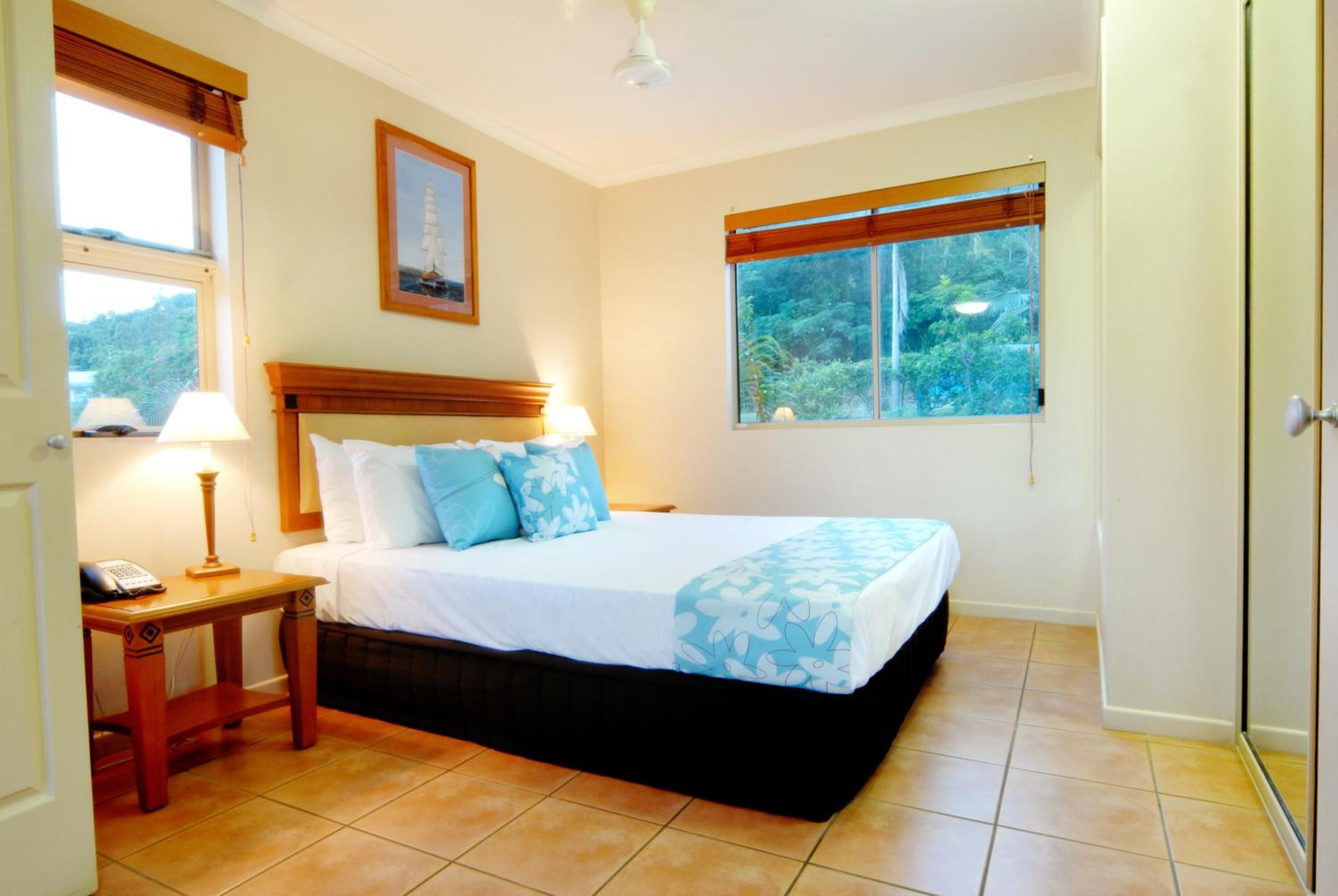 Un dormitorio con cama, mesita de noche, lámpara y ventana con vista a la vegetación.