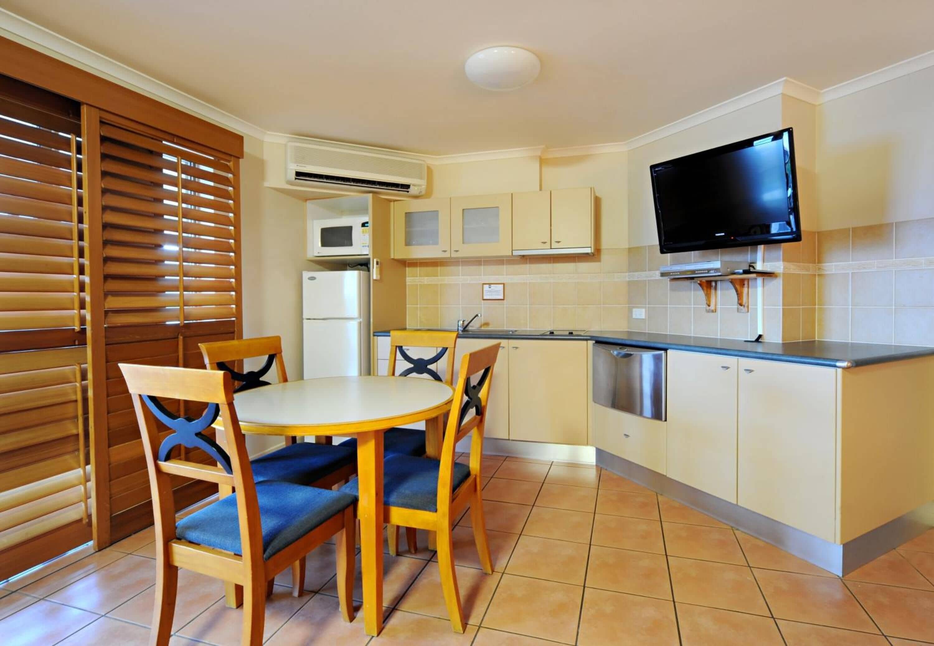 Una cocina compacta con una mesa de comedor, sillas, televisor y refrigerador.