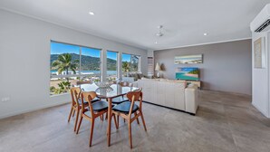 A modern kitchen with a large island, a dining area with a table and chairs, and a view of the beach. - at Boathaven Bay Holiday Apartments (Airlie Beach)