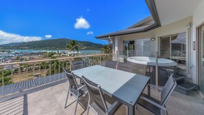 A balcony with a table and chairs, a hot tub, and a view of the sea and mountains. - at Boathaven Bay Holiday Apartments (Airlie Beach)
