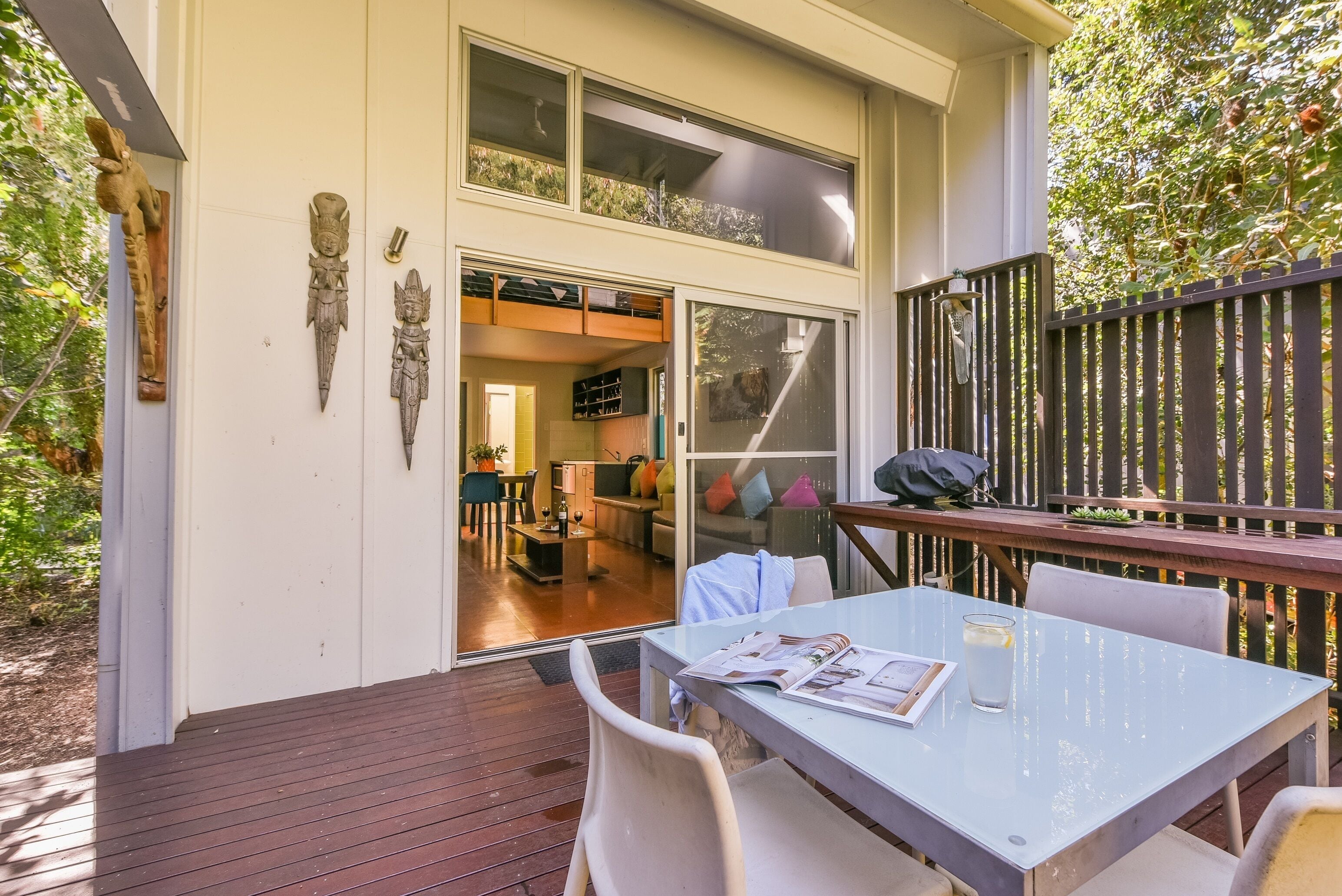 A modern house with a deck, a dining area with a table and chairs, and a sliding glass door leading to an interior space with a kitchen and living area.