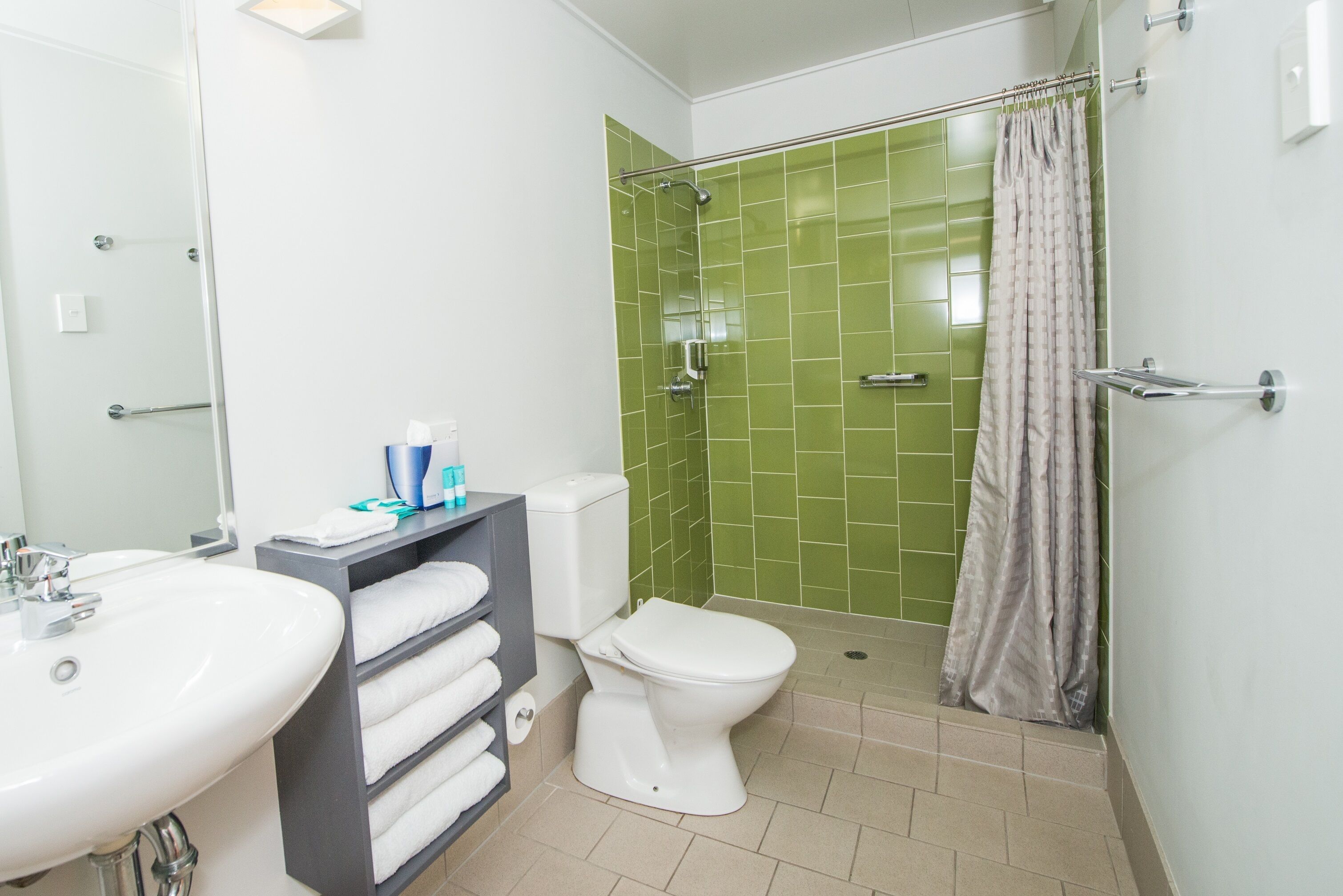 A bathroom with a white sink, a toilet, and a shower with green tiles.