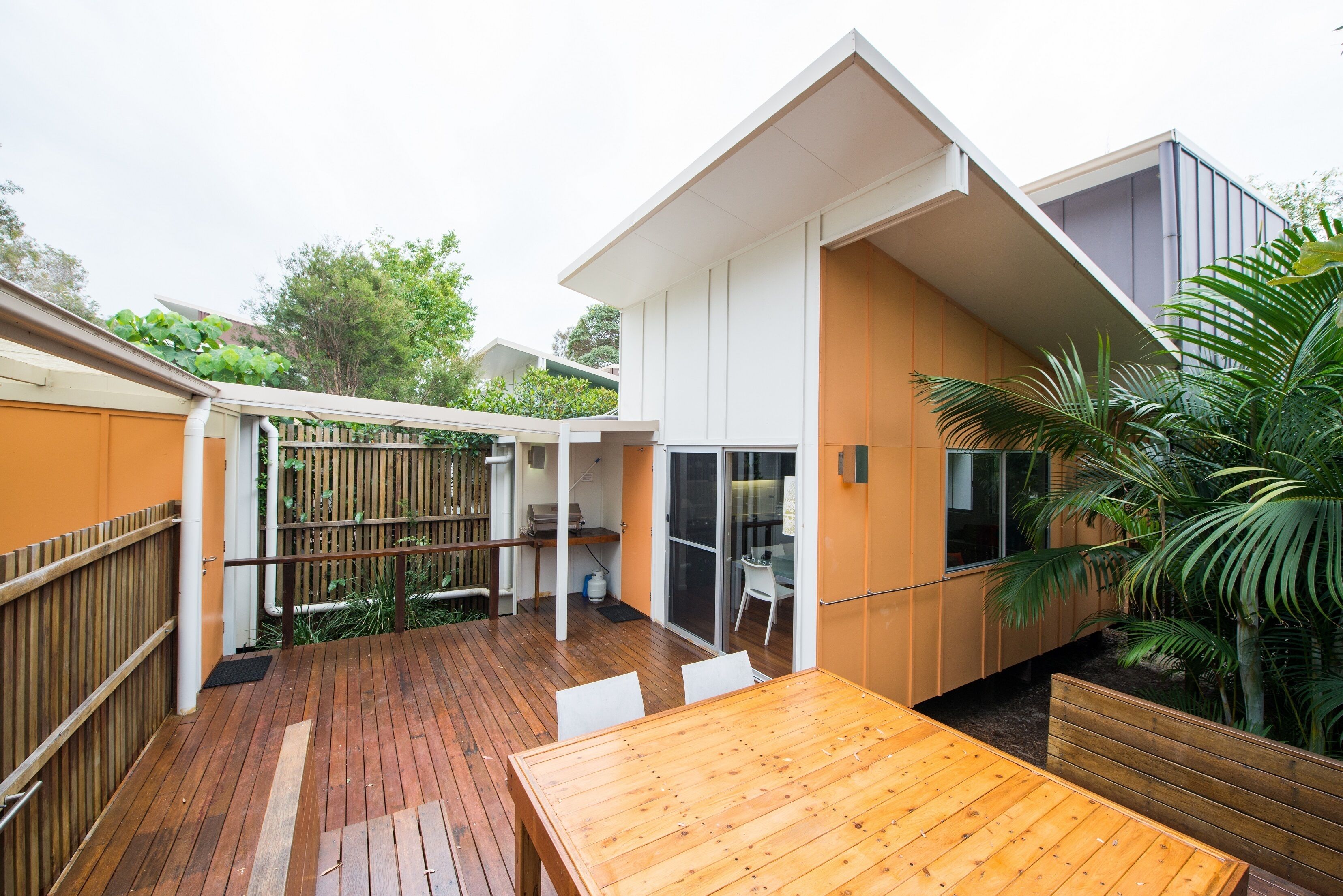 Een modern huis met een houten terras, een eethoek en een overdekt patio.
