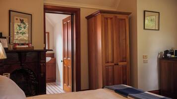 A hotel room with a bed, wooden wardrobe, a desk with a lamp, and a framed botanical print on the wall.
