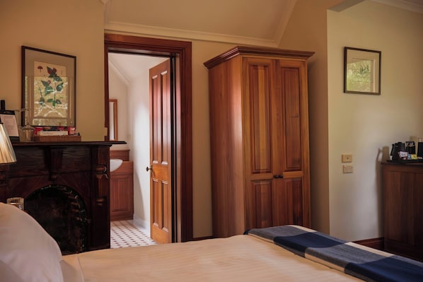 Habitación de hotel con cama, armario de madera, un escritorio con lámpara e impresión botánica enmarcada en la pared.