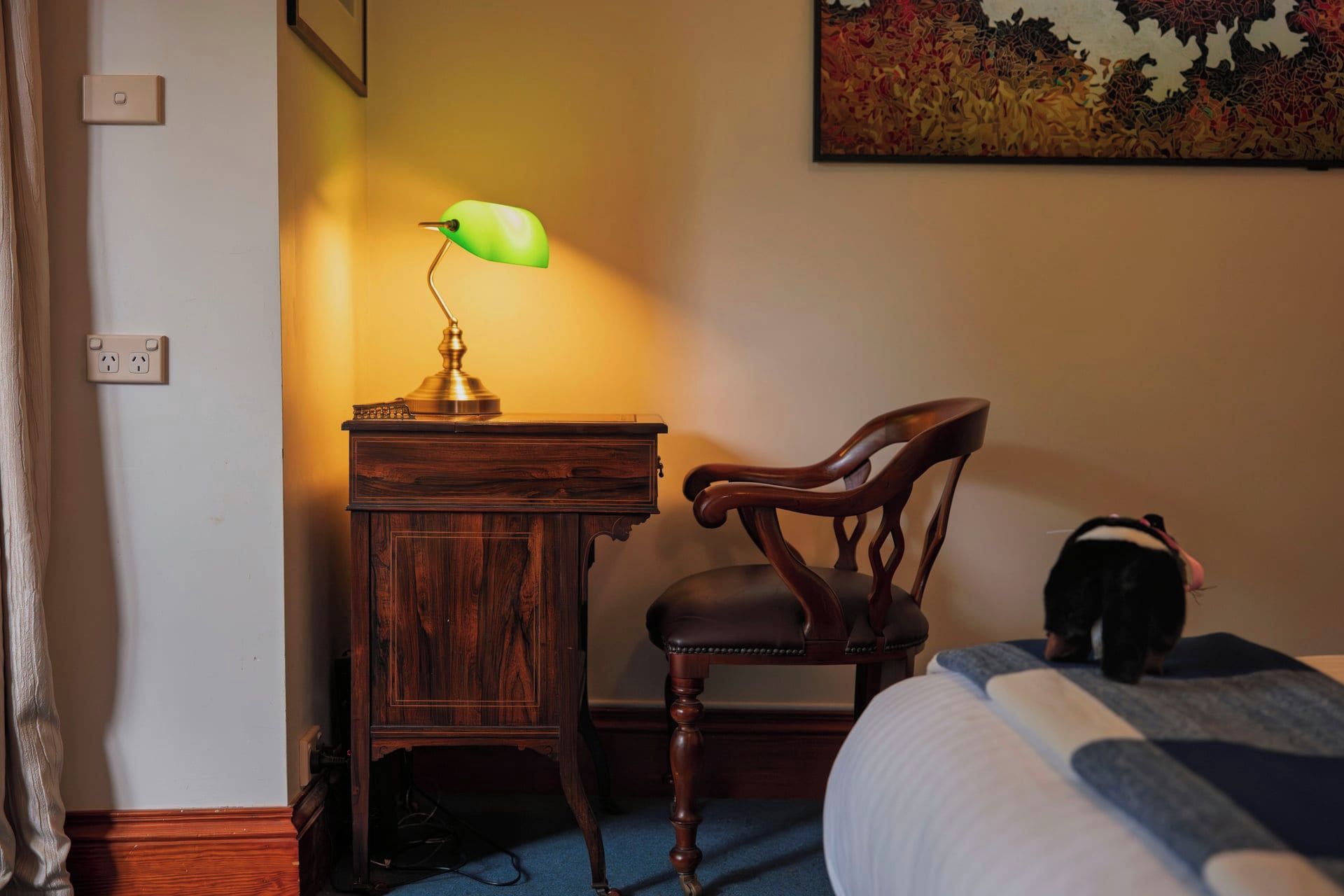 Ein Holztisch mit Lampe, ein Stuhl und ein Bett mit Decke.