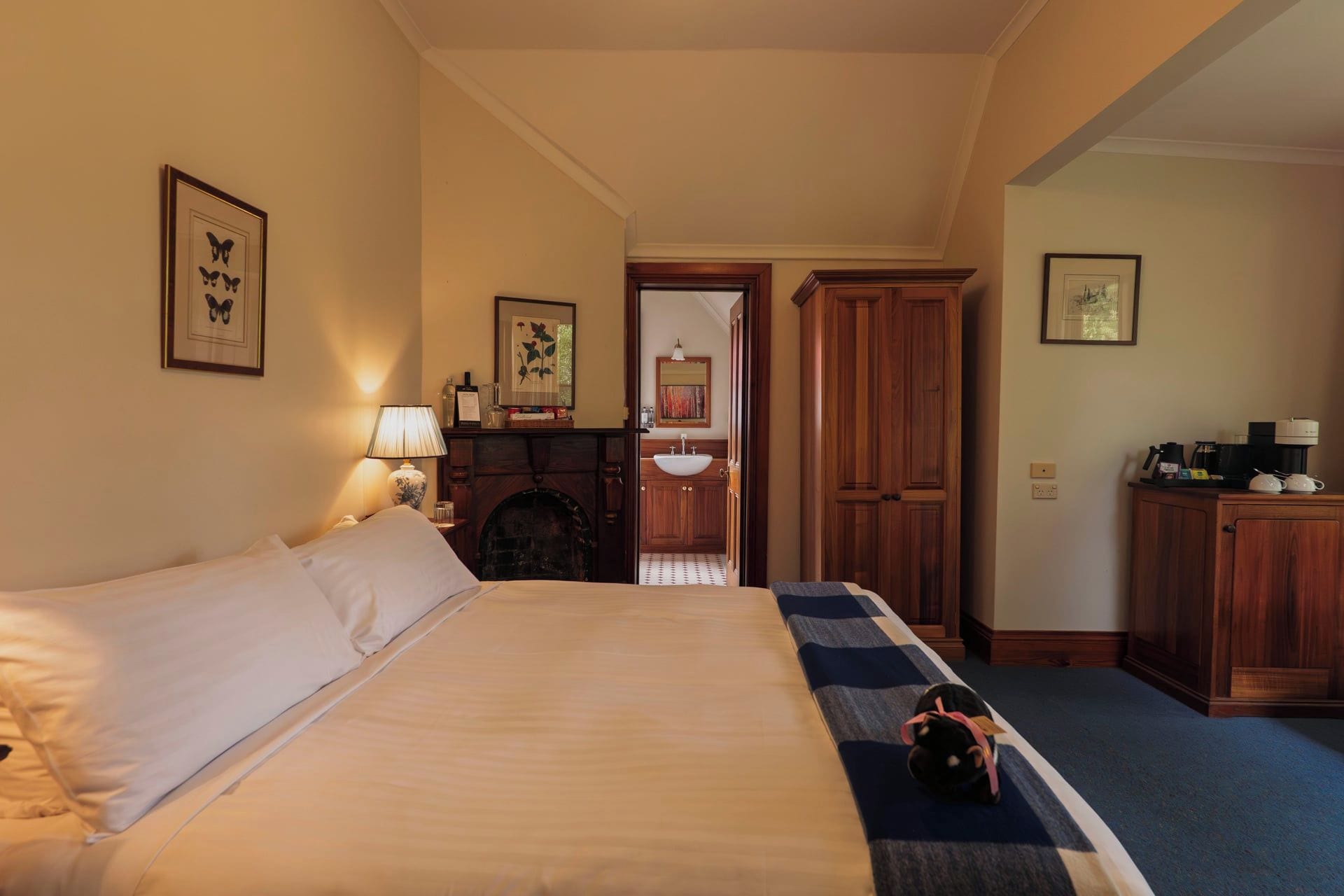 Une chambre d’hôtel avec un lit, une lampe, une cheminée, un bureau avec une machine à café et un petit tapis.