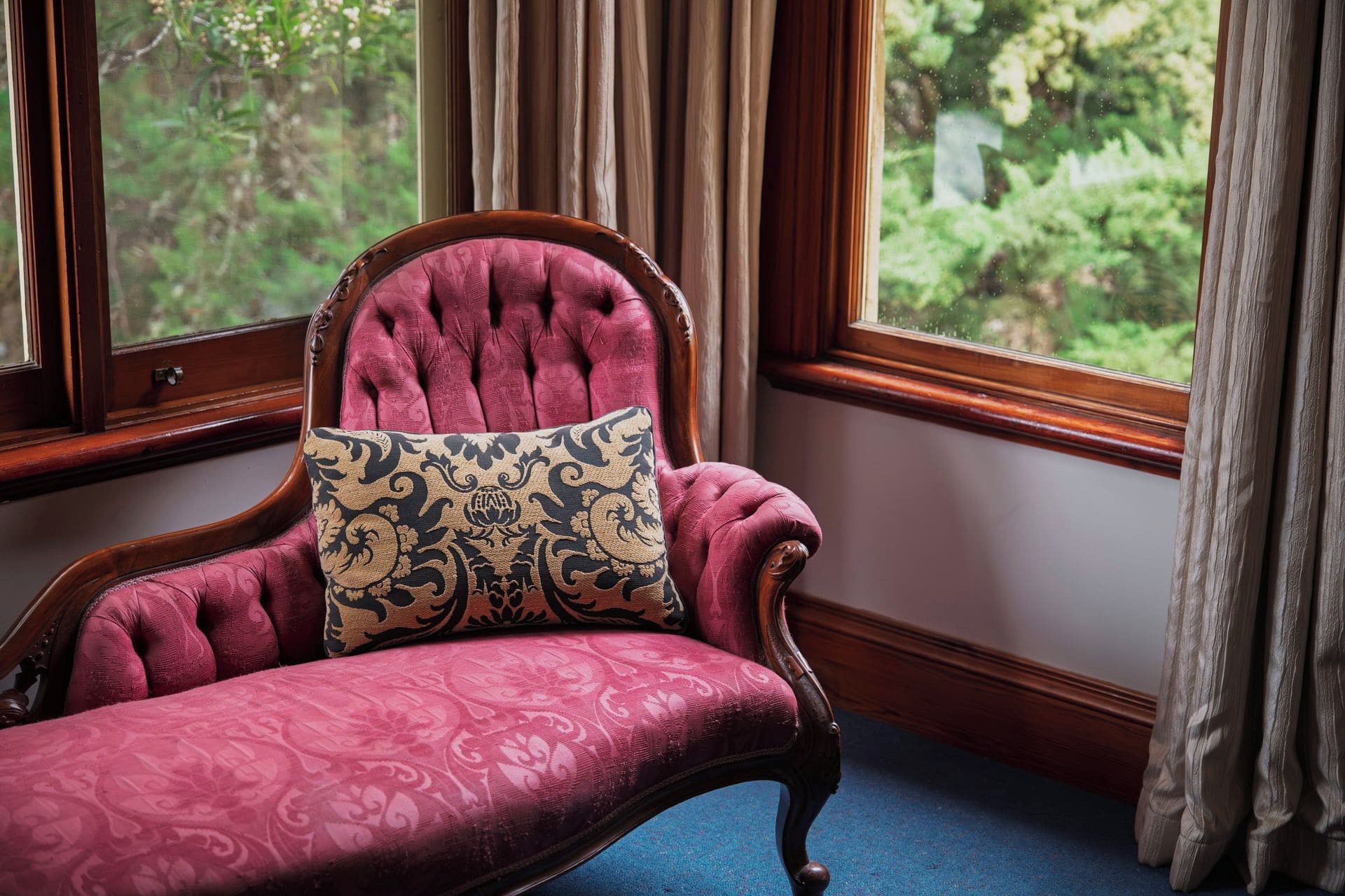 A chair with a patterned cushion in a room with a window and curtains.