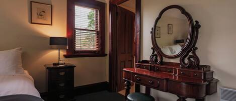 A bedroom with a bed, a dresser with a mirror, a bedside table with a lamp, and a window with blinds.