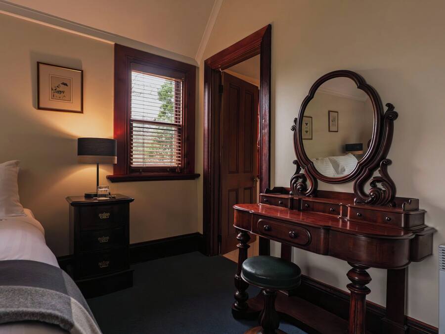 A bedroom with a bed, a dresser with a mirror, a bedside table with a lamp, and a window with blinds.