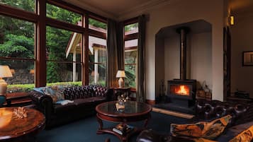 Un salón acogedor con chimenea, mobiliario de cuero y ventanas amplias con vistas a un jardín.
