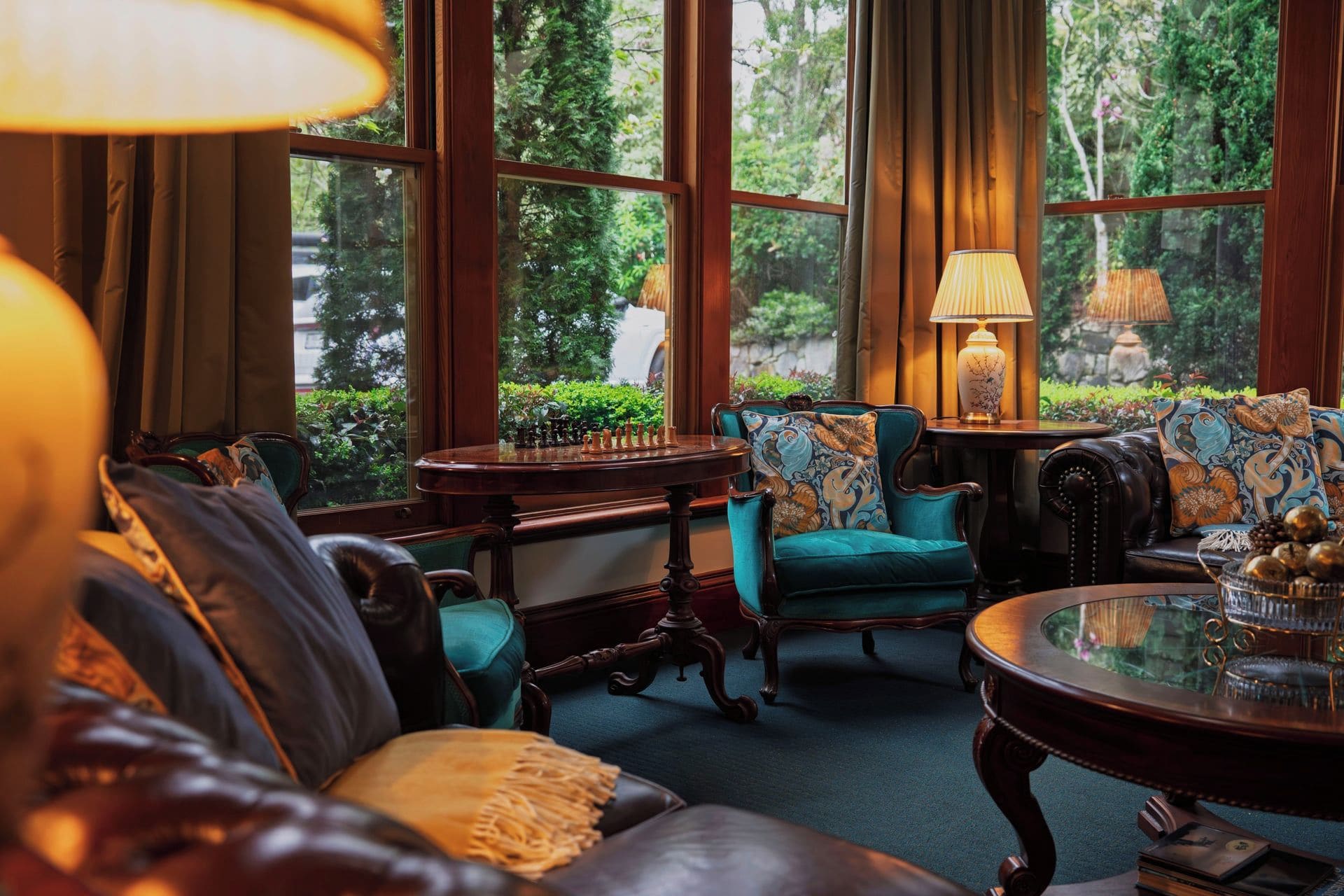 A cozy room with a chess table, plush seating, and a view of greenery.