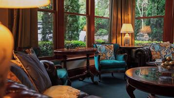 A cozy room with a chess table, plush seating, and a view of greenery.