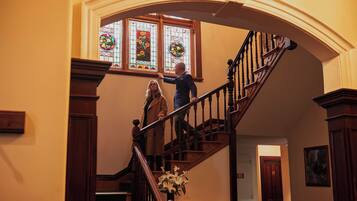A grand staircase with a wooden handrail and balusters, leading to a landing with a stained glass window above.