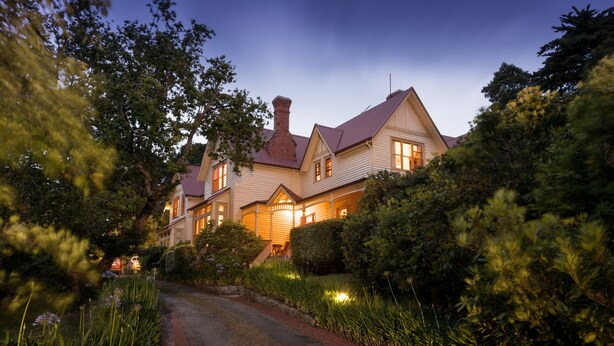 A large, two-story house with a prominent chimney, surrounded by lush greenery and a paved driveway. - Franklin Manor (Strahan)