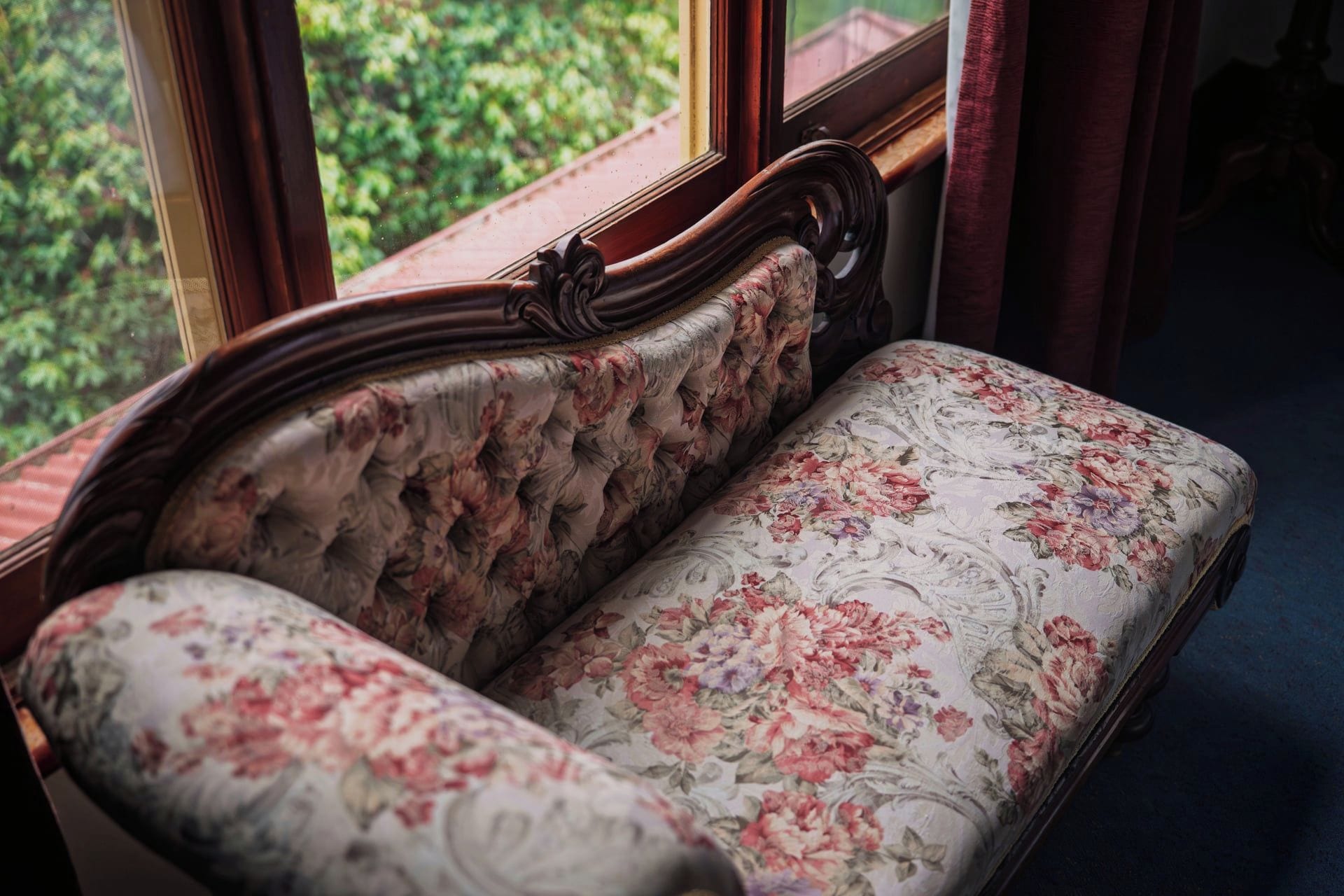 A vintage sofa with floral upholstery in a room with a window.