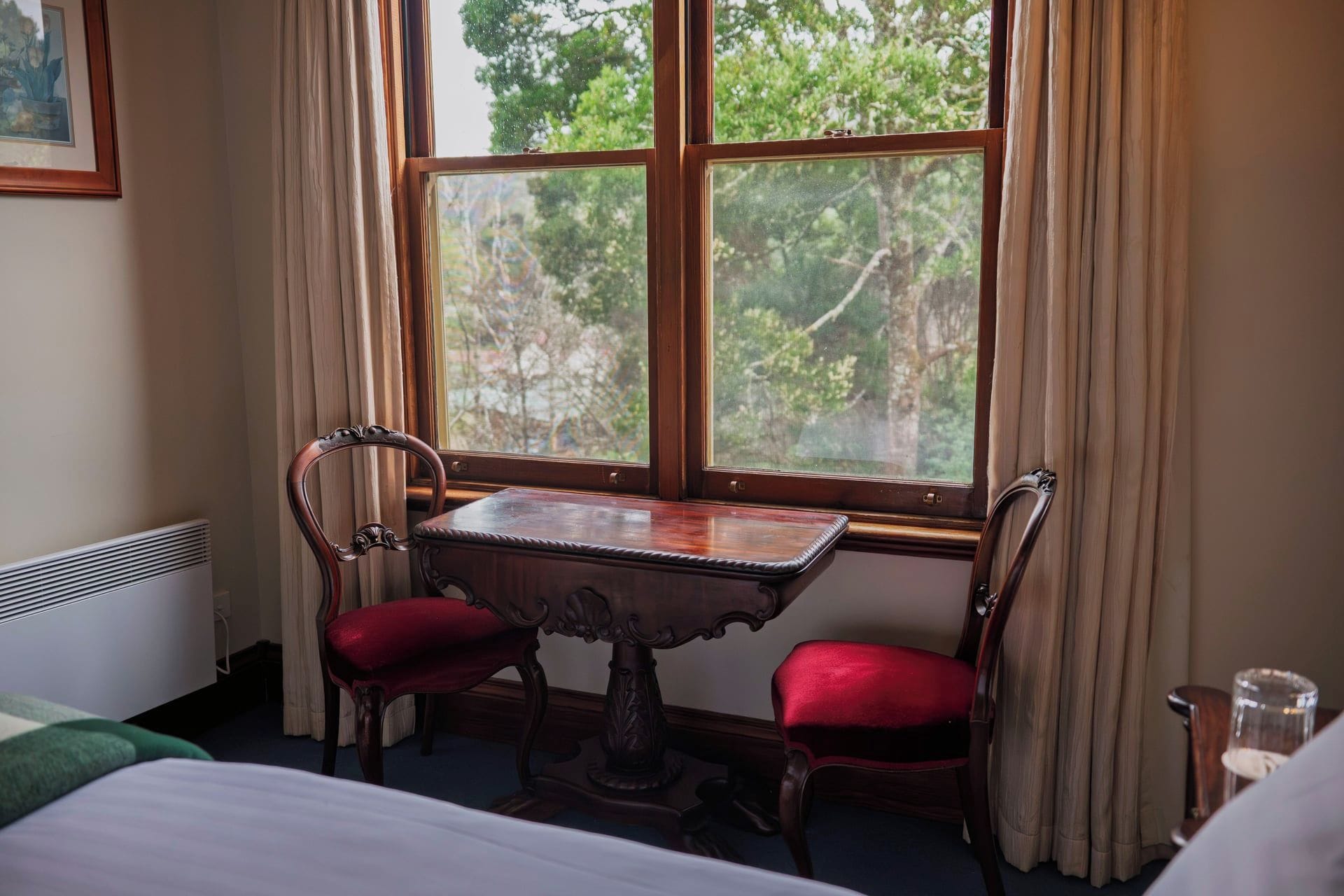 Una habitación con una mesa de madera y dos sillas, un radiador y una ventana con cortinas.