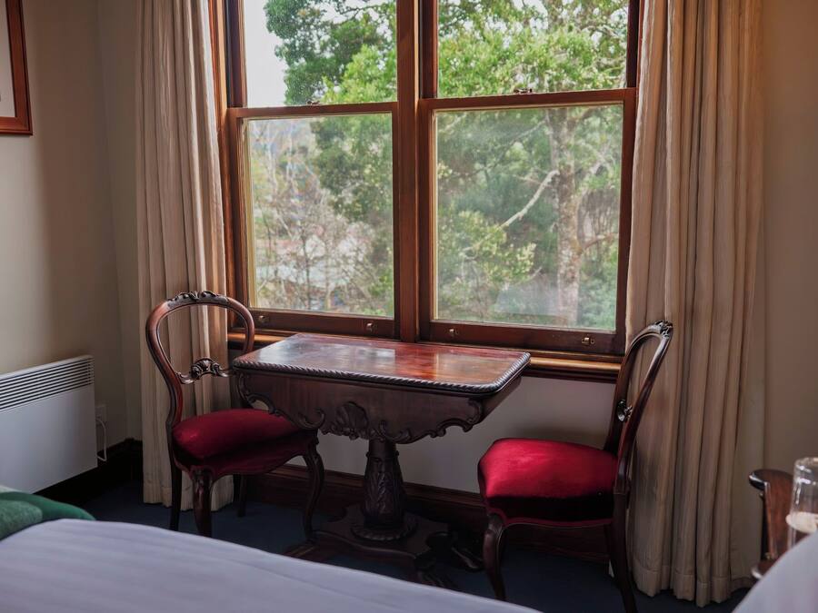 Una habitación con una mesa de madera y dos sillas, un radiador y una ventana con cortinas.