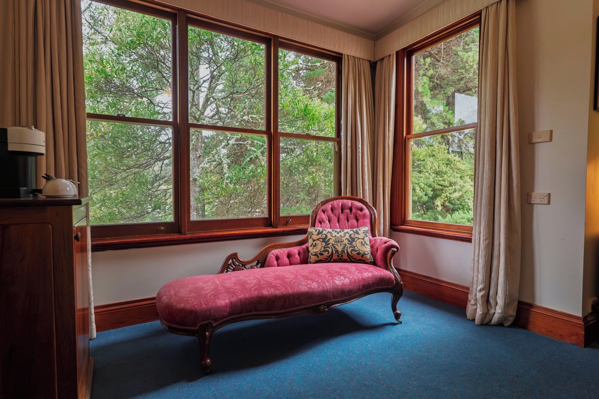 Quarto com uma janela grande, um banco estofado vermelho e um armário de madeira.