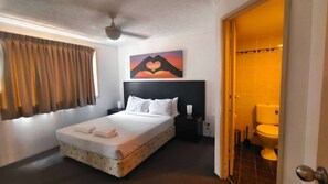 A hotel room with a bed, a nightstand, a wall-mounted artwork, and a bathroom visible through an open door.