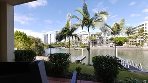A view from a balcony overlooking a river, with palm trees and a modern building complex in the background. - K Resort (Surfers Paradise)