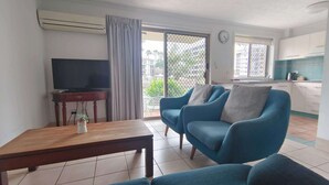 A living room with a TV, a wooden table, and a blue sofa. - K Resort (Surfers Paradise)