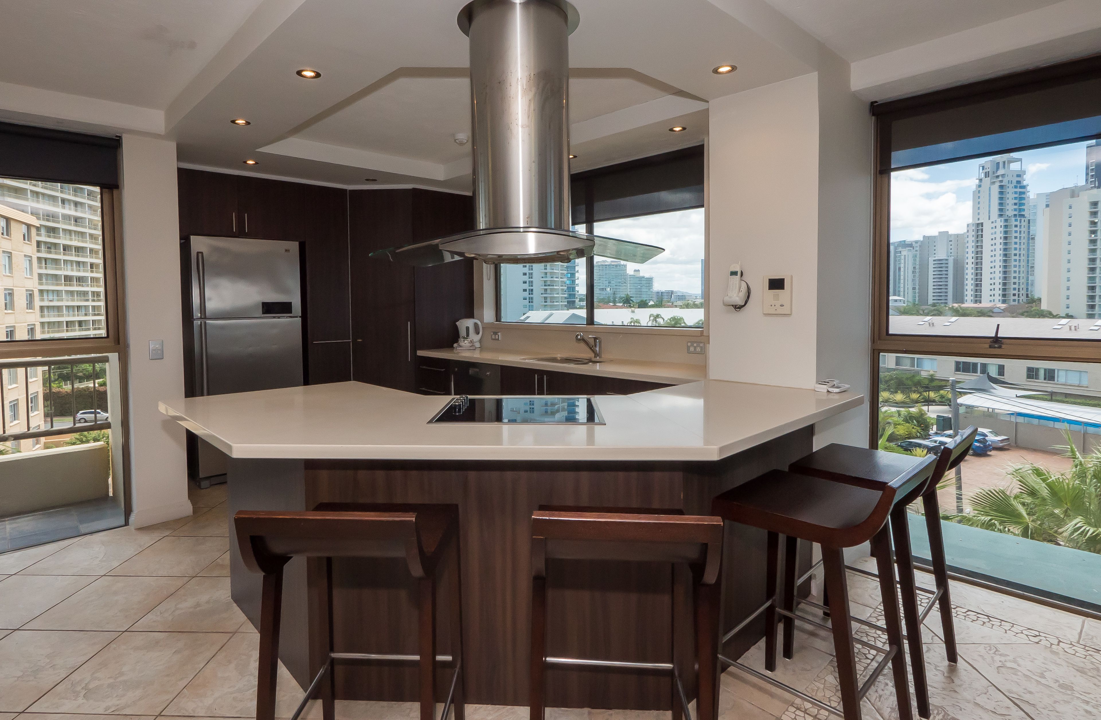 Una cocina moderna con una isla grande, armarios de madera oscura, electrodomésticos de acero inoxidable y un amplio ventanal con vista a la ciudad.
