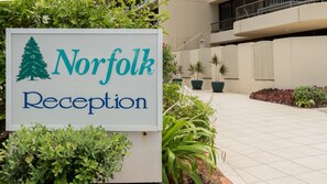 A reception sign for Norfolk with a tree logo, surrounded by greenery and potted plants. - Norfolk Luxury Beachfront Apartments (Main Beach)