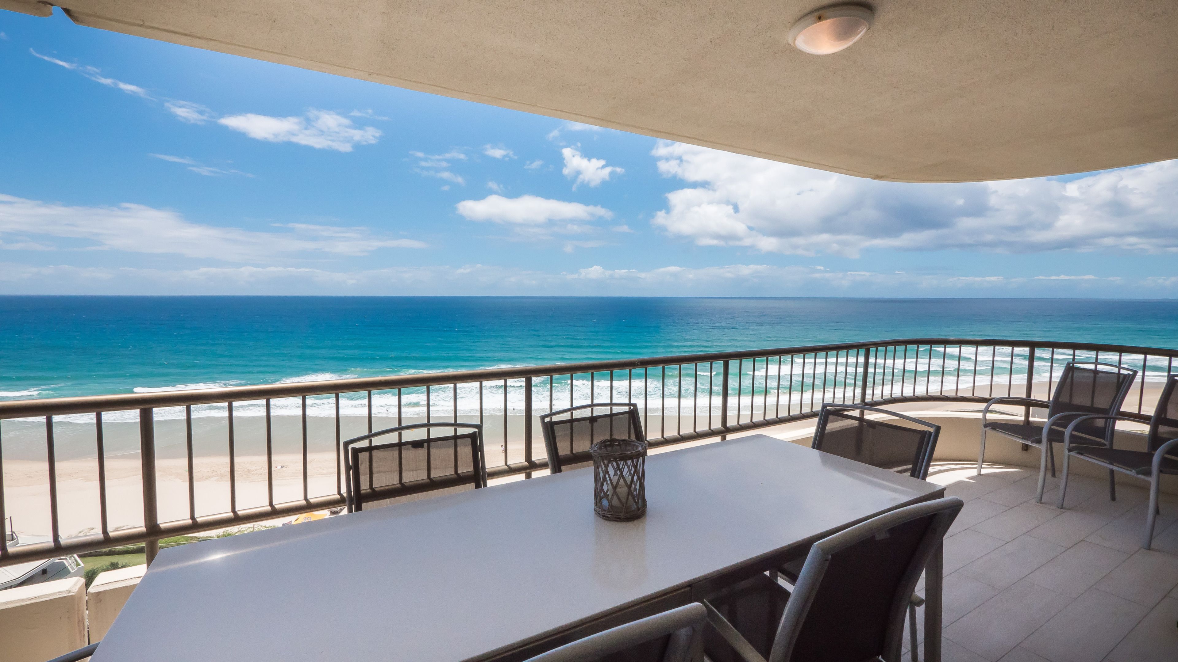 Ein Balkon mit Tisch und Stühlen mit Blick auf einen Strand und das Meer.