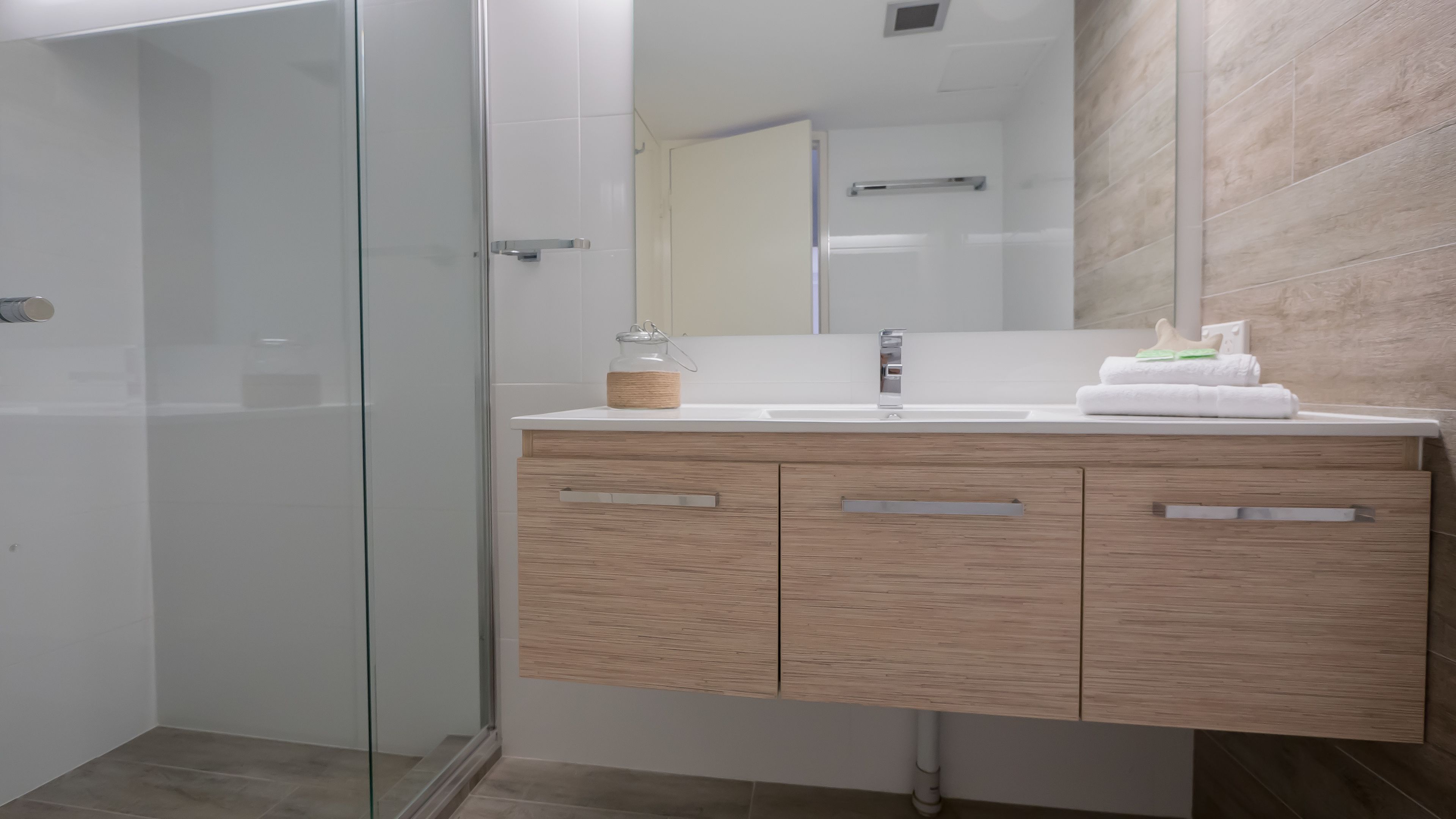 A modern bathroom with a glass shower enclosure, a wooden vanity with a mirror, and a towel rack.