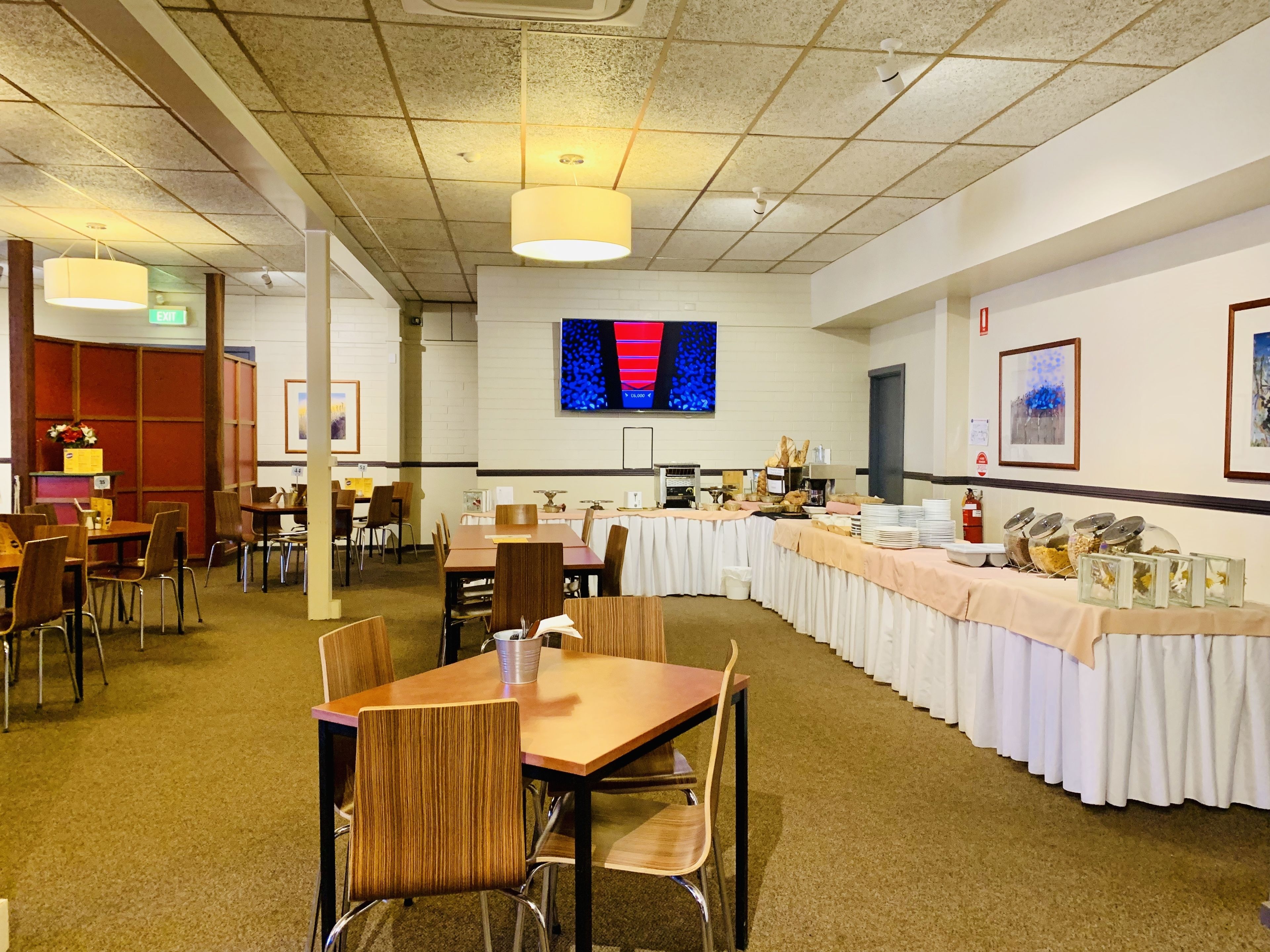 Un salón de conferencias con una larga mesa, sillas, una pantalla de televisión y una mesa de buffet.