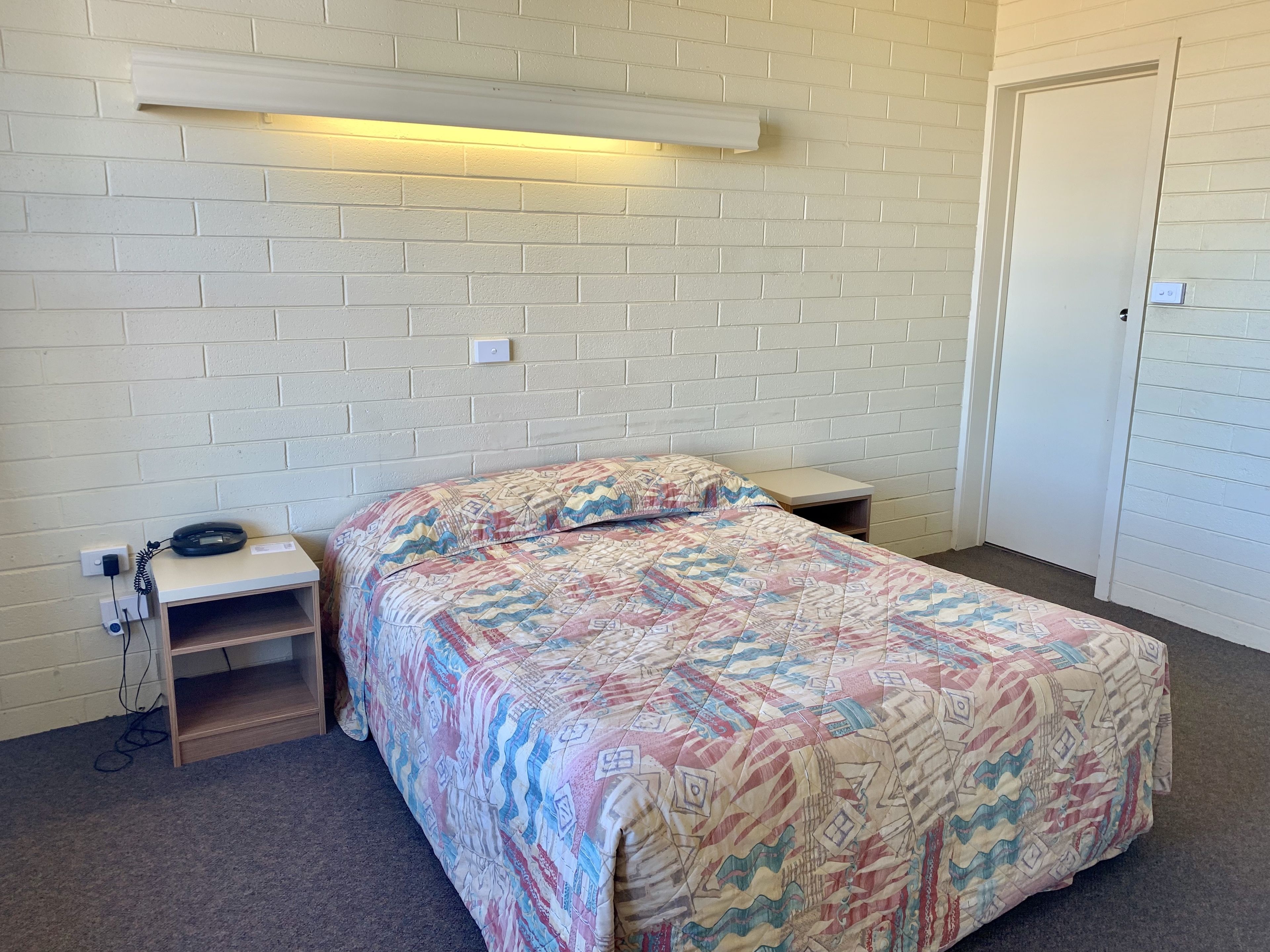 A bedroom with a bed, a bedside table, a lamp, and a door.