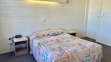 A bedroom with a bed, a bedside table, a lamp, and a door.
