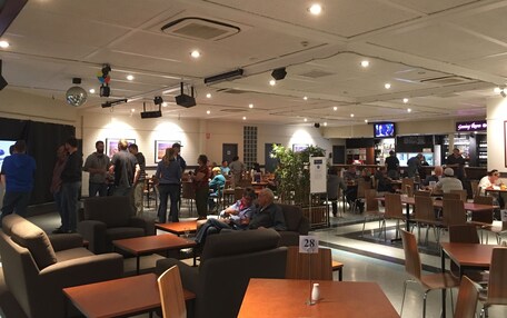 A spacious indoor area with multiple seating arrangements, including tables and chairs, and a bar area in the background.