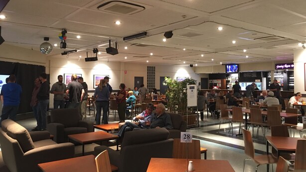 Un grand espace intérieur aménagé avec différents types de sièges, notamment des tables et des chaises, et un bar situé au fond de la pièce.