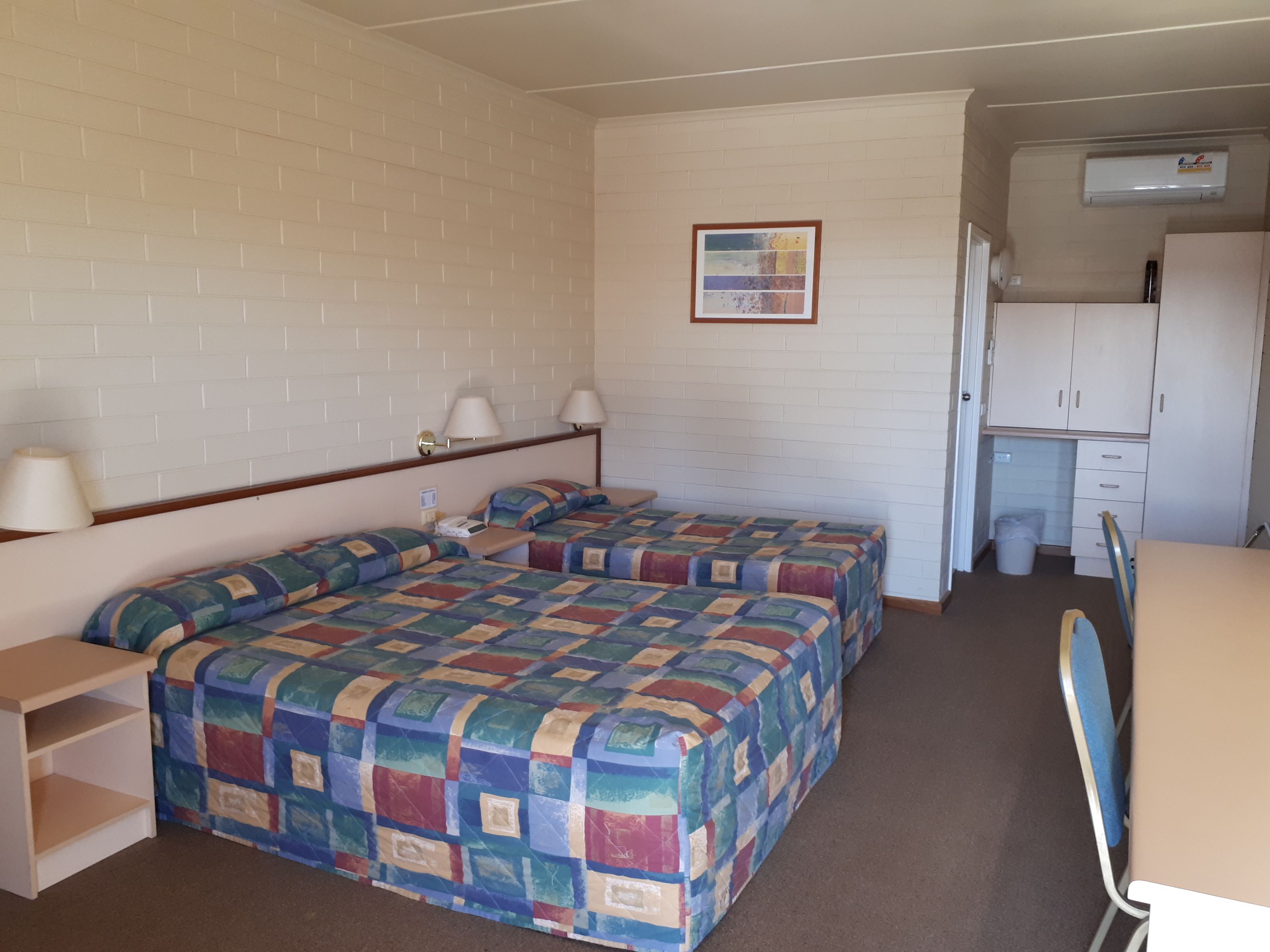 Een kamer met twee bedden, een bureau, een stoel, een klein tafeltje, een kast en een foto aan de muur.