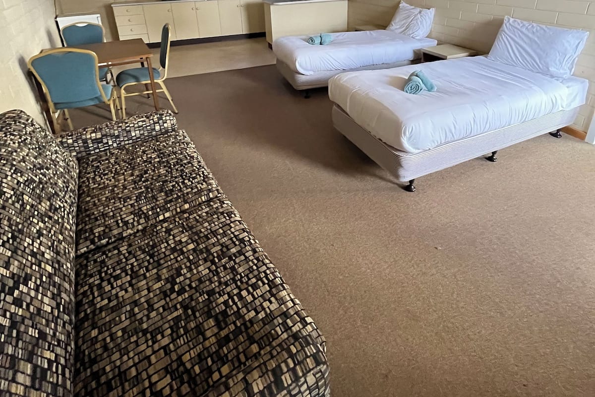 A hotel room with a patterned sofa, two single beds, a small kitchenette, and a dining area with a table and chairs.