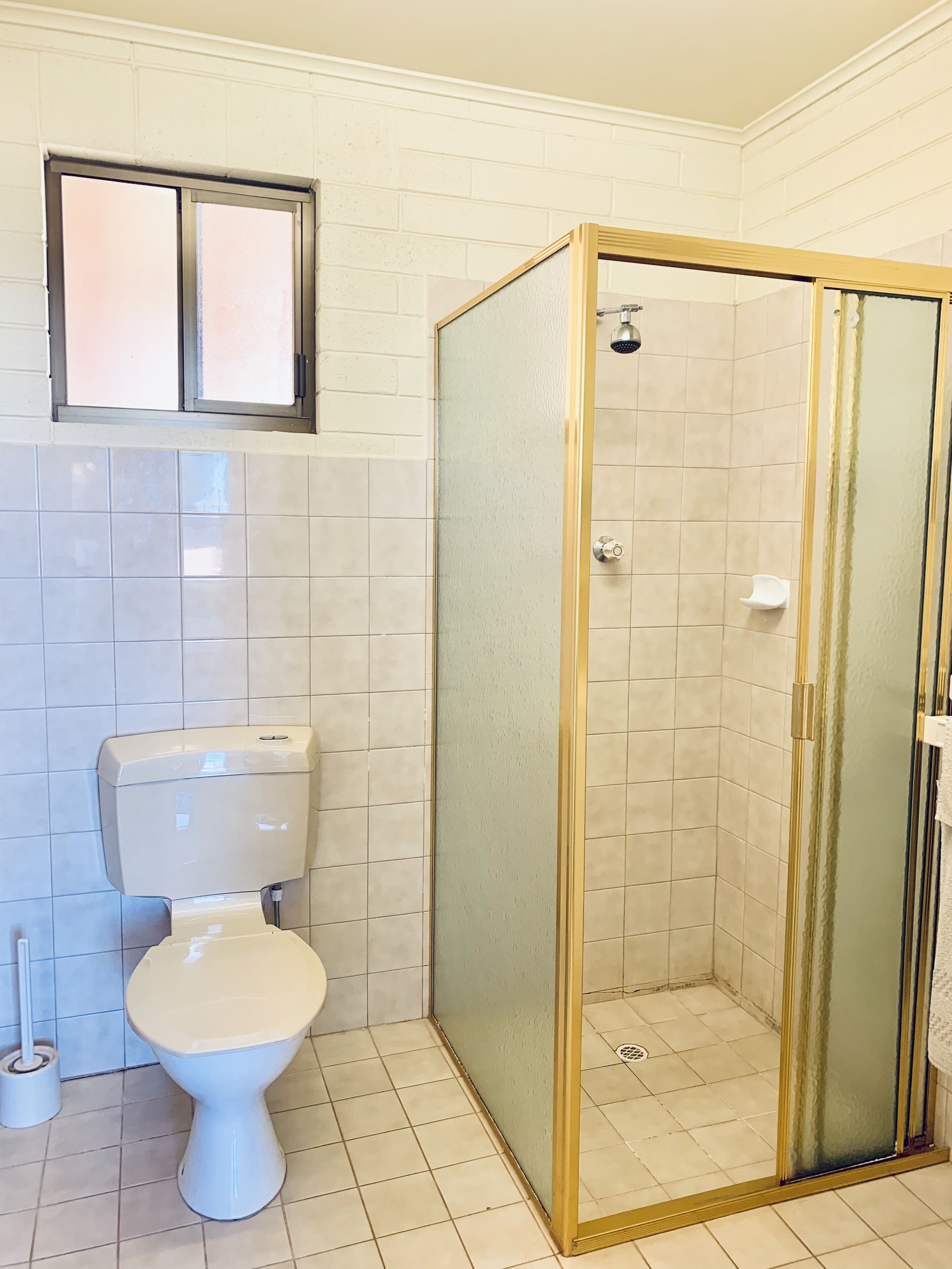 A bathroom with a toilet, a shower enclosure, and a window above the toilet.