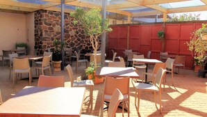 Une terrasse extérieure avec des tables et des chaises, des murs en pierre et des plantes en pot.