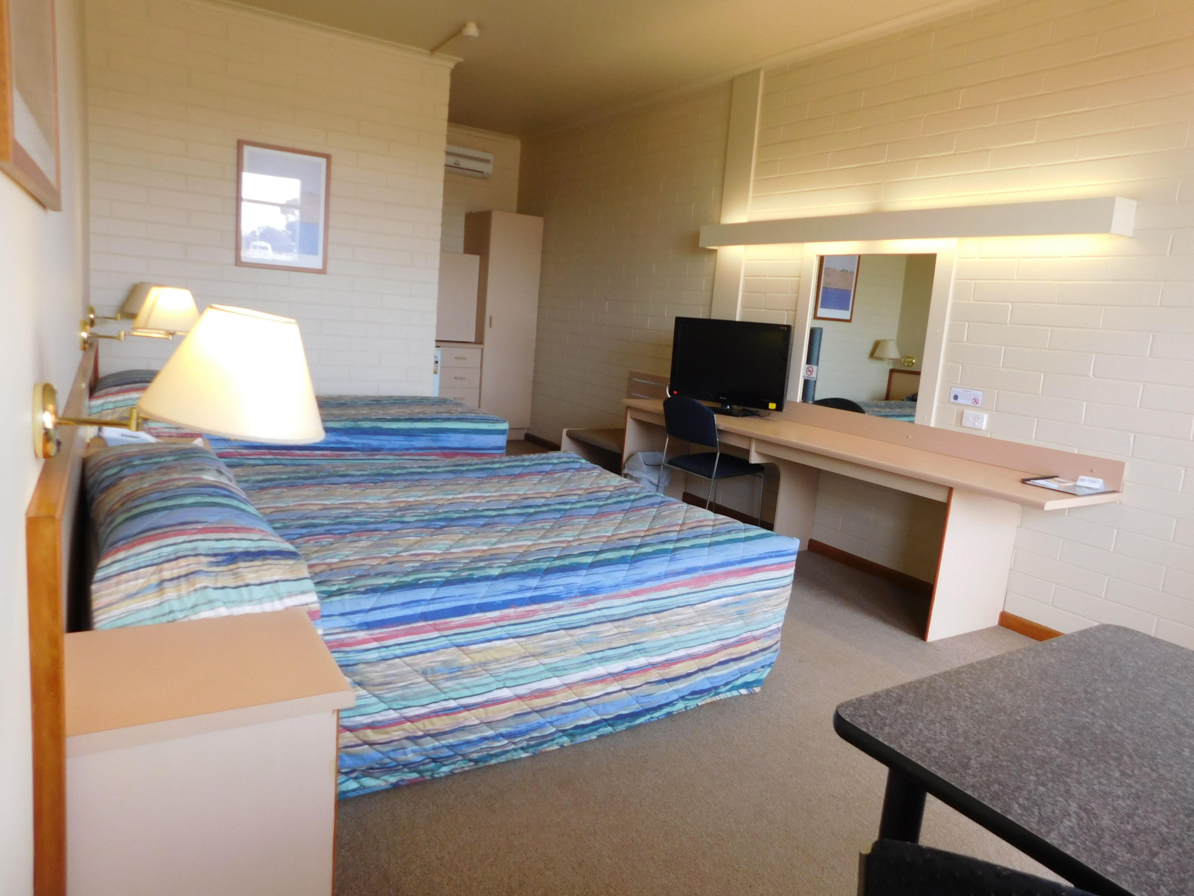 Ett hotellrum med två sängar, ett skrivbord, en stol, en tv och en spegel.