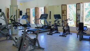 Un gimnasio con diversas máquinas de ejercicio, amplias ventanas y una puerta que da al exterior.