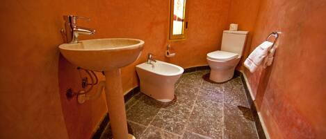 Une salle de bain équipée d’un lavabo, d’un bidet, de toilettes et d’une fenêtre donnant sur un paysage agréable.