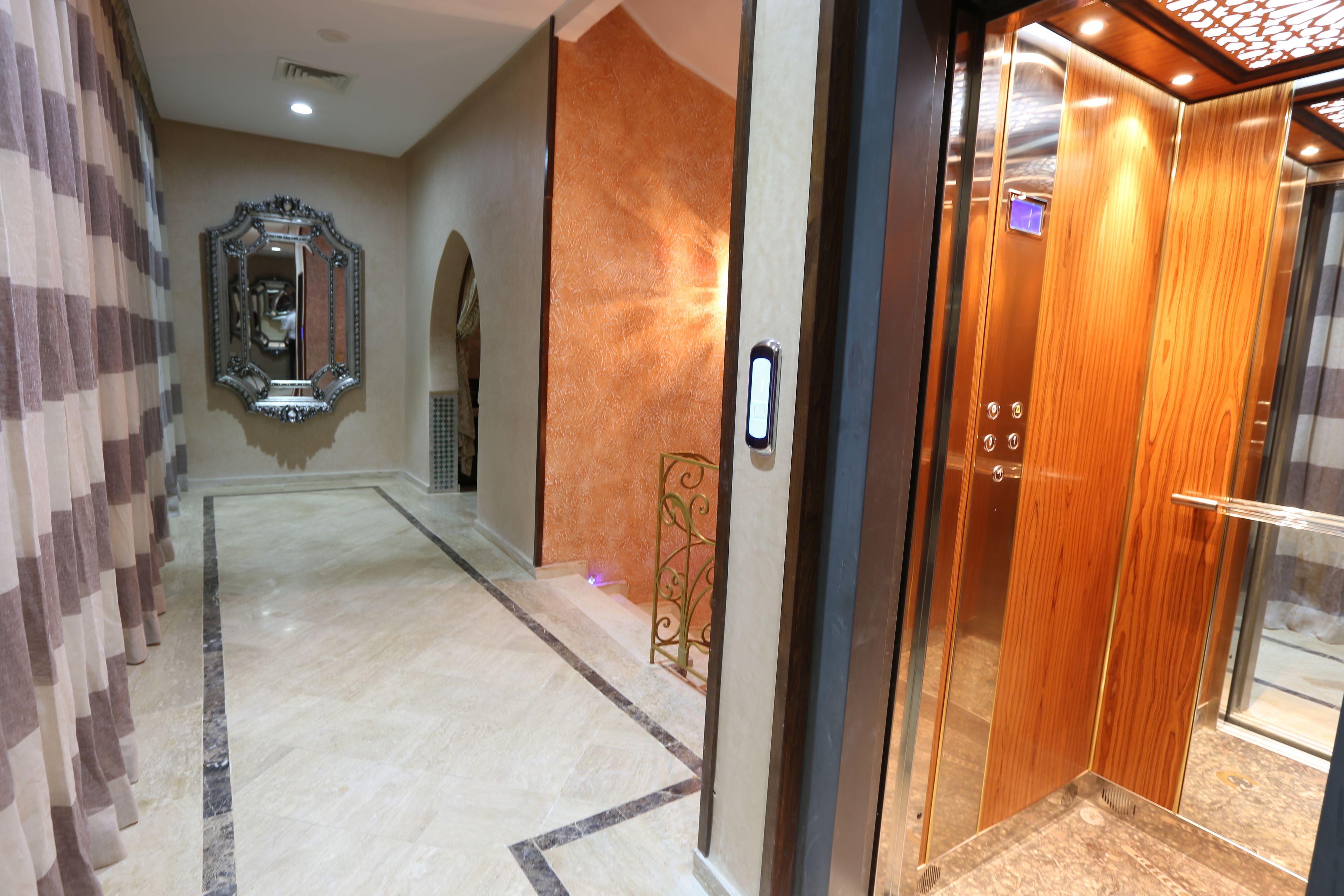 A hallway with a marble floor, a mirror, and an elevator with a wooden finish.