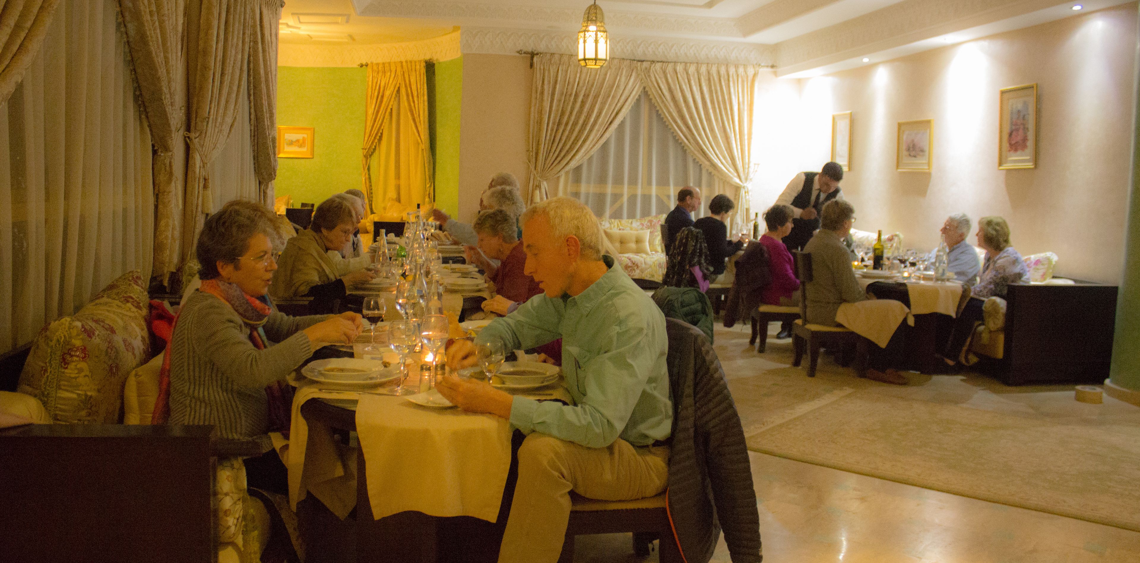A dining area with multiple tables set for a meal, featuring a variety of table settings and guests.